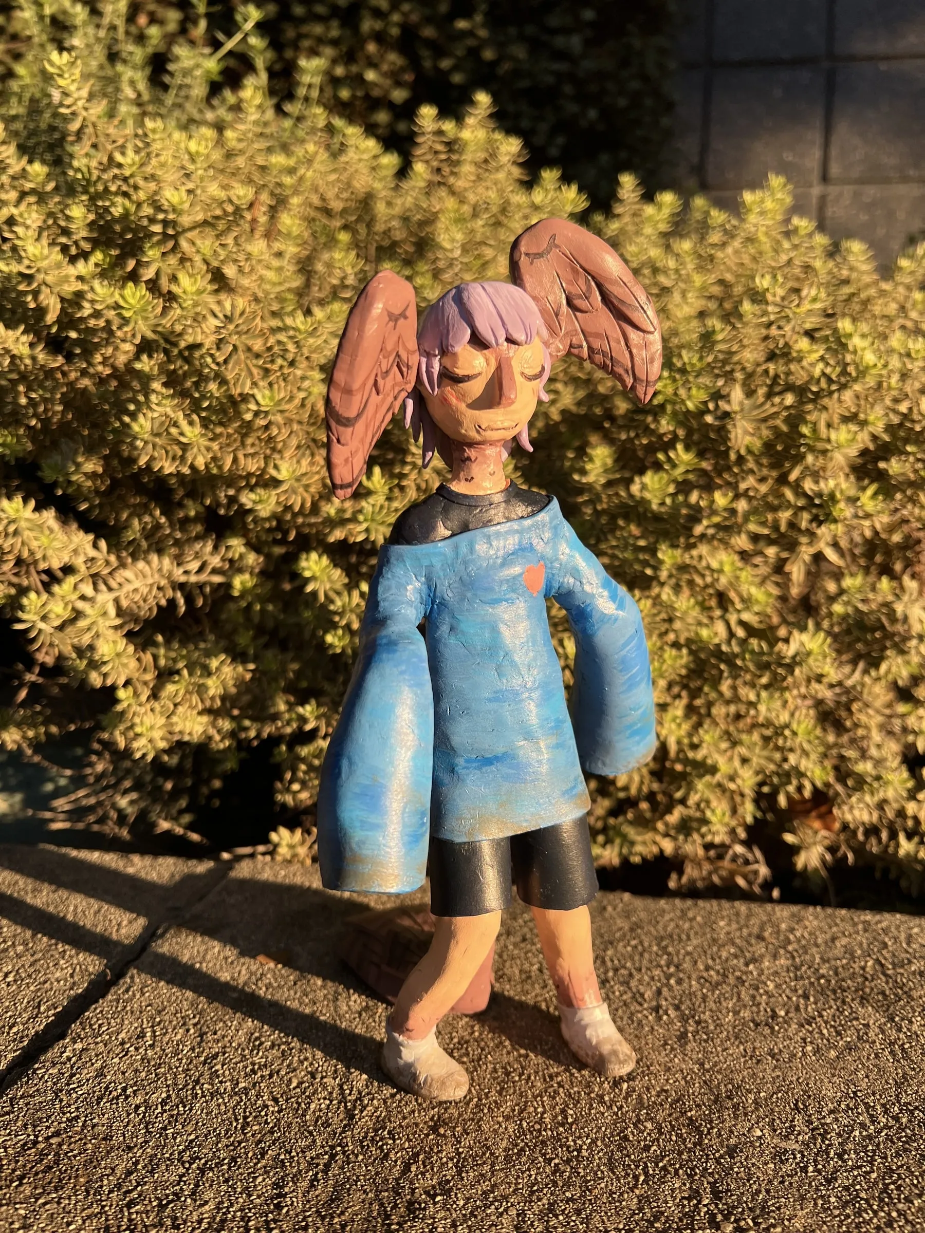 Painted sculpture of Rin standing, wings folded, photographed outdoors